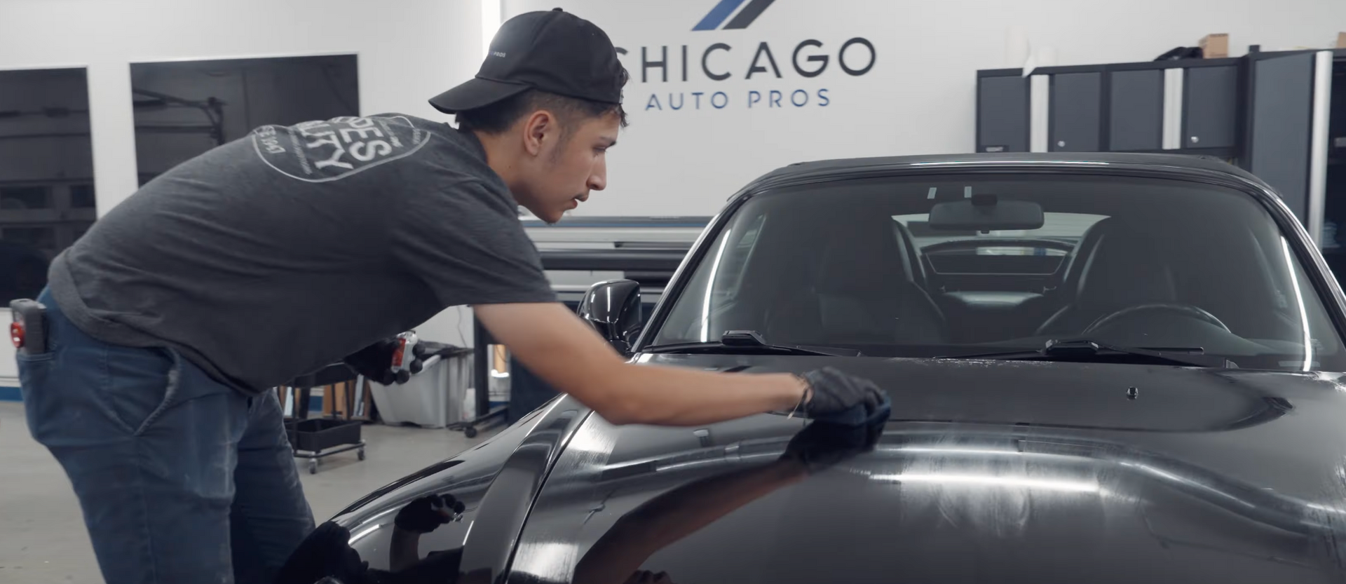 A man is cleaning the hood of a car in a garage.