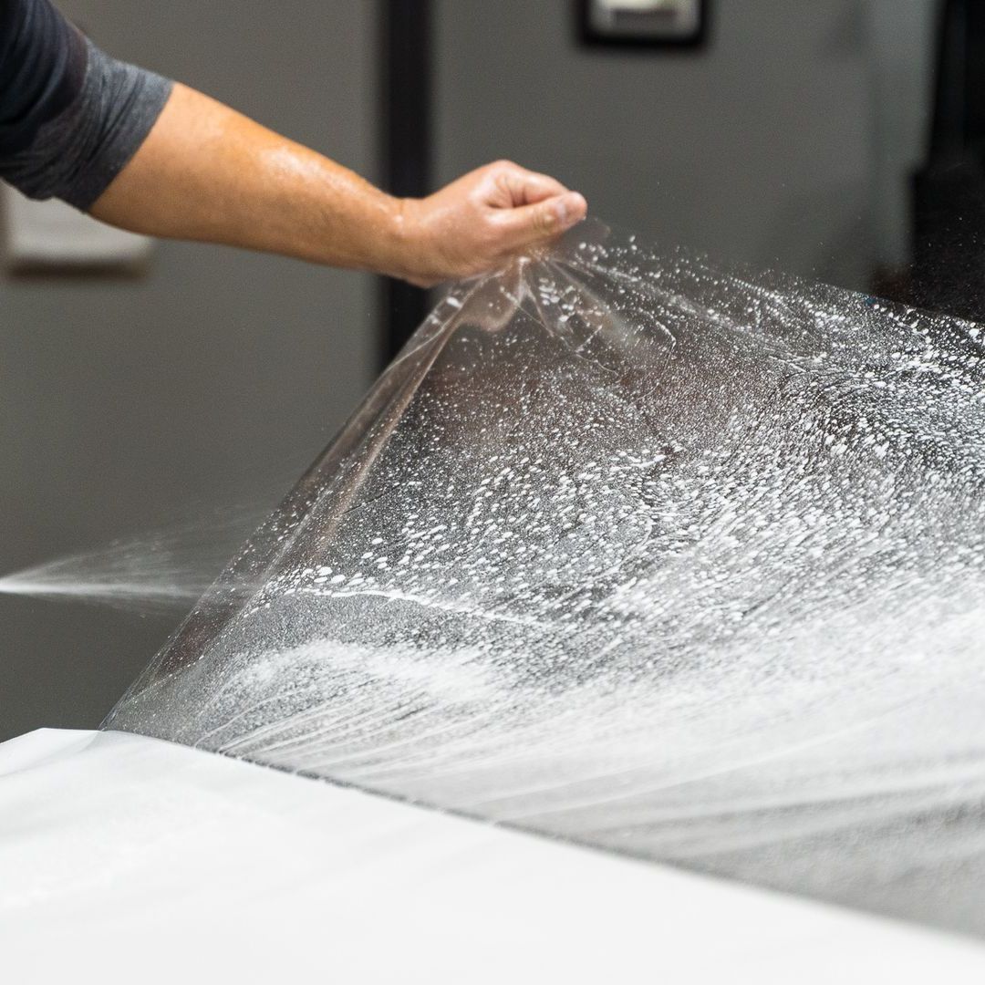 A person is holding a piece of plastic over a car.
