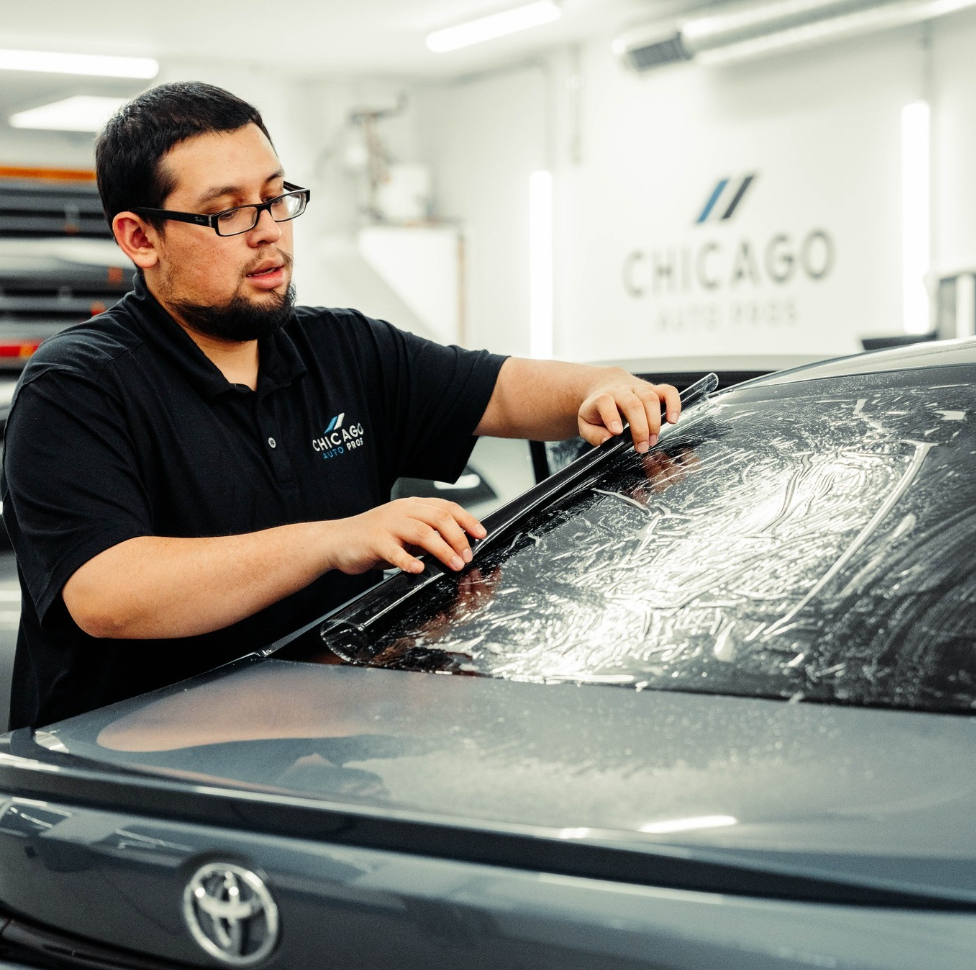A man is cleaning the windshield of a car in front of a sign that says chicago