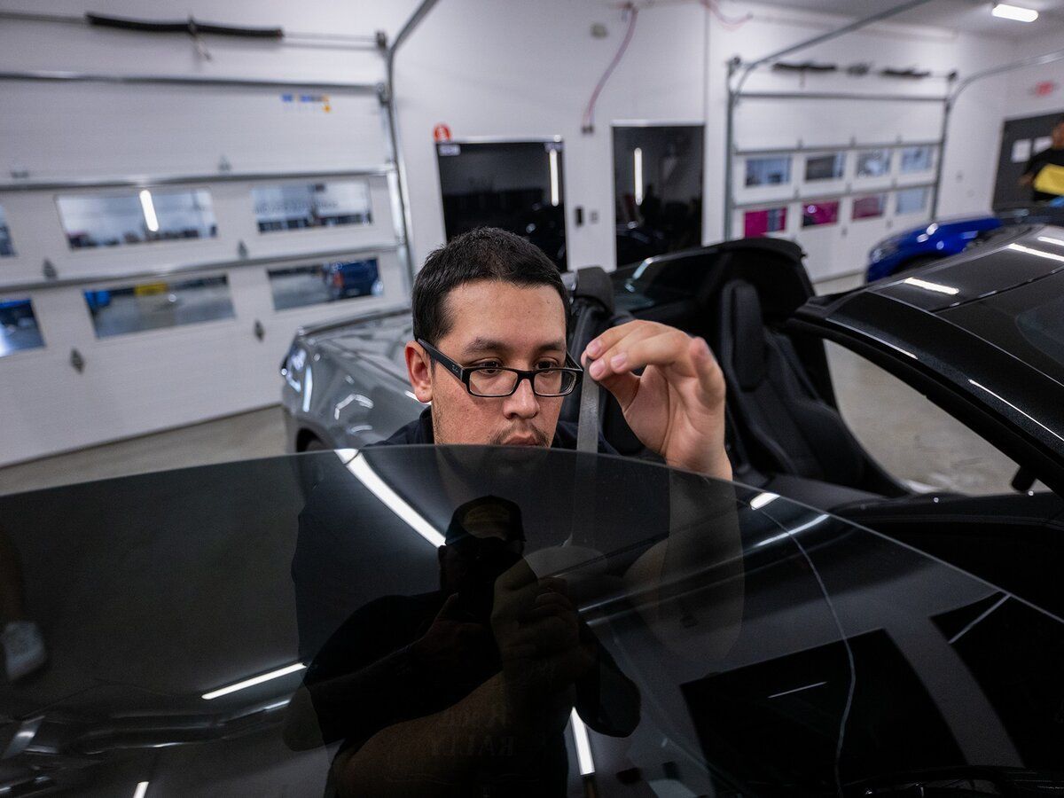 A man wearing glasses is working on the windshield of a car.