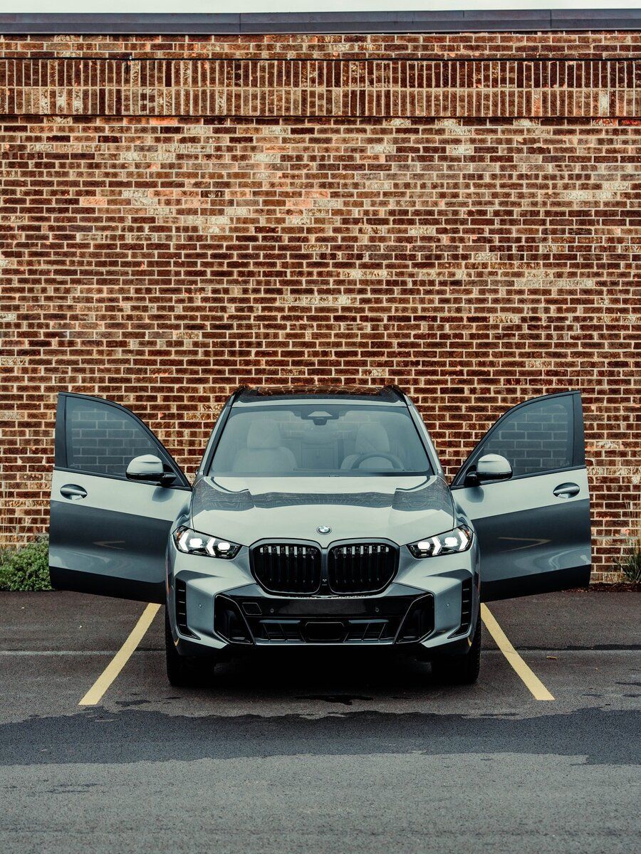 A car is parked in a parking lot with its doors open in front of a brick wall.