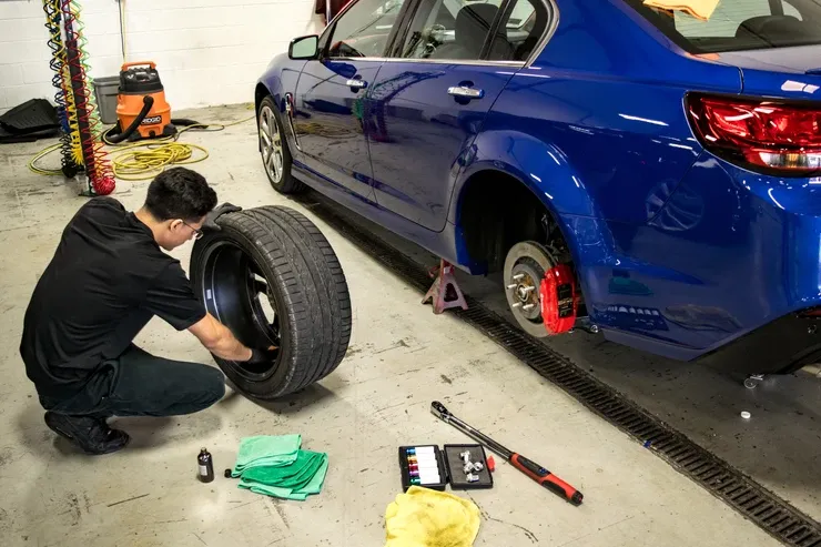 A man is changing a tire on a blue car in a garage.