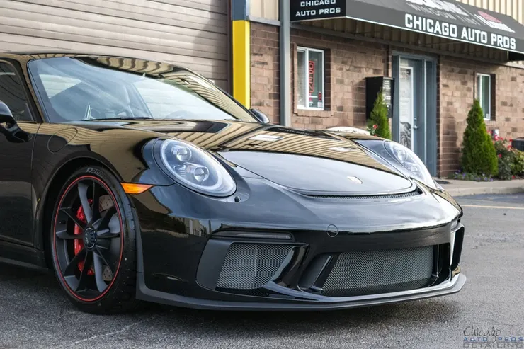 A black porsche 911 gt3 is parked in front of a chicago auto parts store.