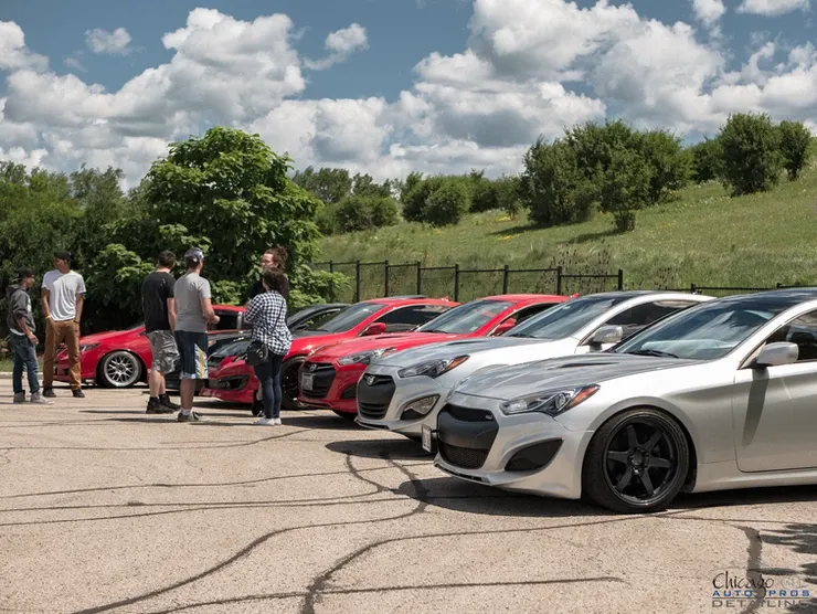 A group of people are standing around a row of cars in a parking lot.