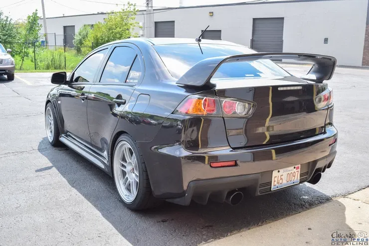 A black car with a spoiler on the back is parked in a parking lot.