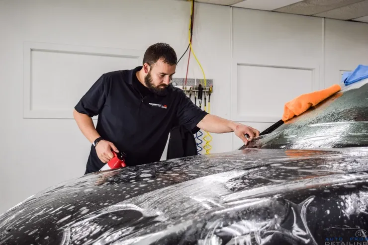 A man is wrapping a car with plastic wrap in a garage.