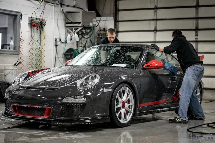 Two men are washing a black sports car in a garage.