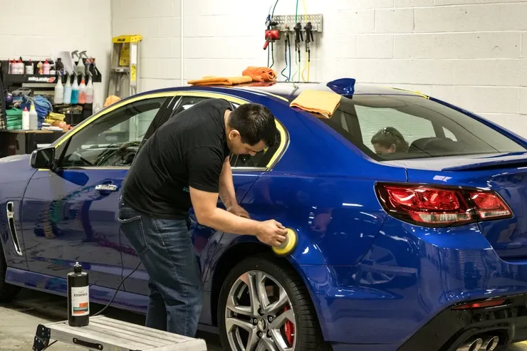 A man is polishing a blue car in a garage.