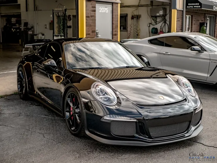 A black porsche 911 gt3 rs is parked in a parking lot next to a white mustang.