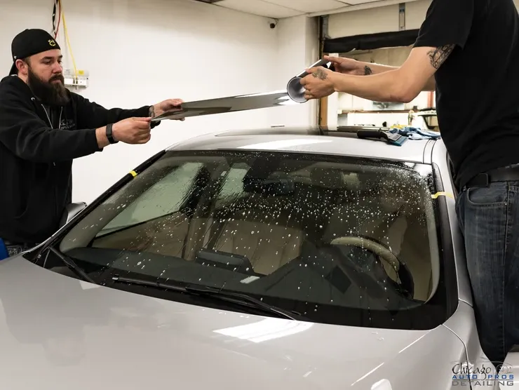 Two men are working on a car windshield in a garage.