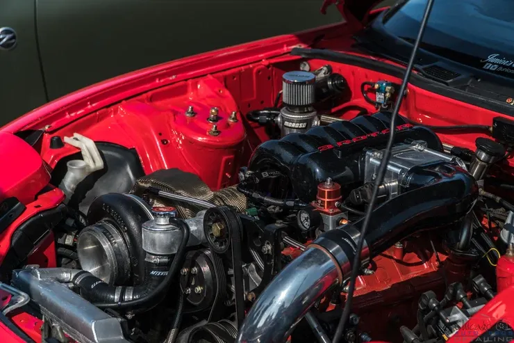 The engine of a red car is shown with the hood open.