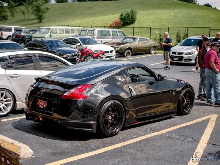A group of people are standing around a black sports car parked in a parking lot.