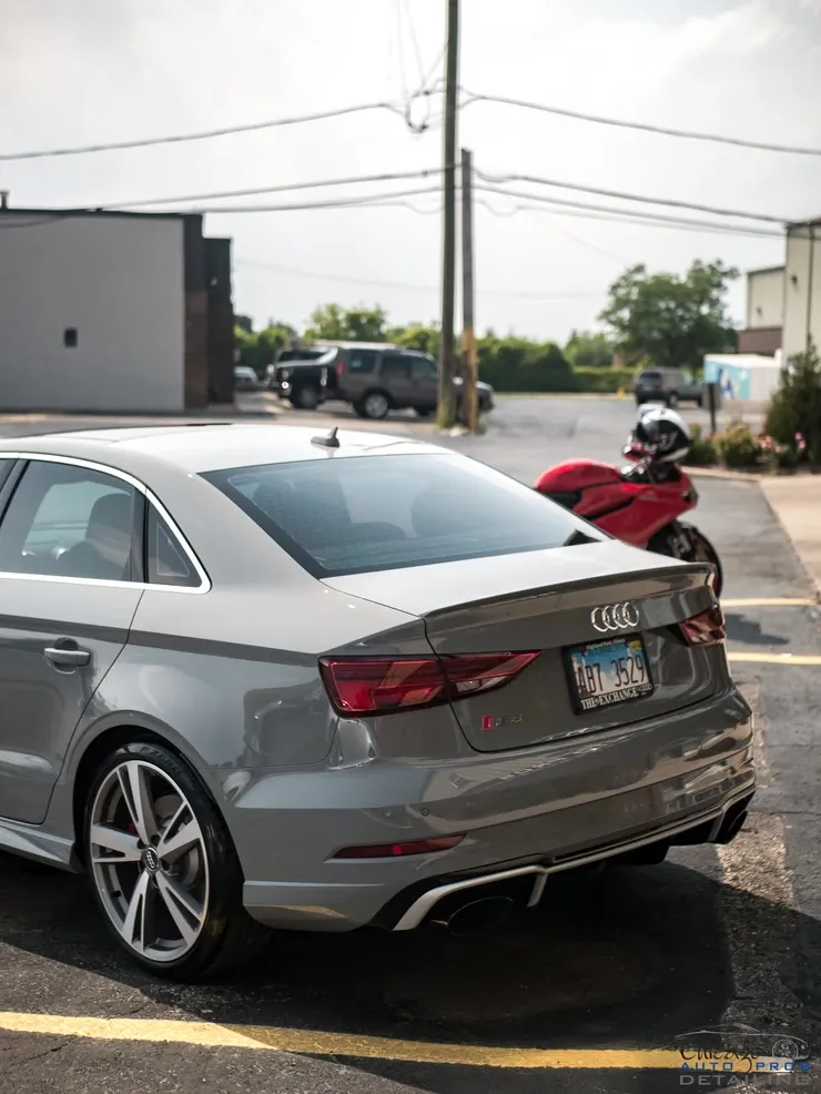 A gray audi a3 is parked in a parking lot next to a red motorcycle.