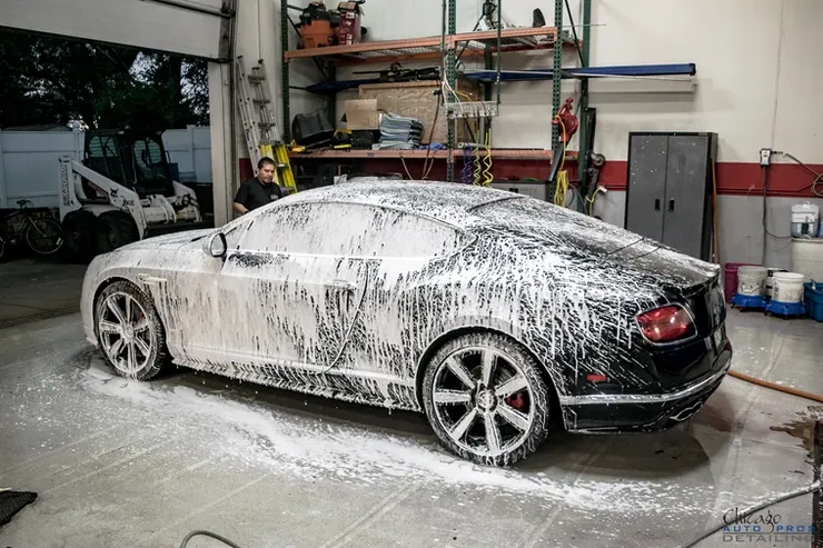 A bentley continental gt is covered in foam in a garage.