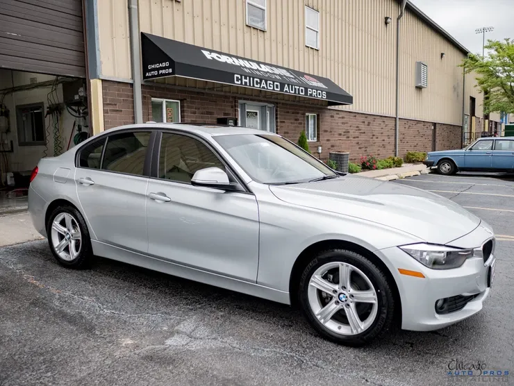 A silver bmw 3 series is parked in front of a building.