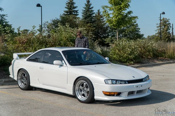 A man is standing next to a white car in a parking lot.