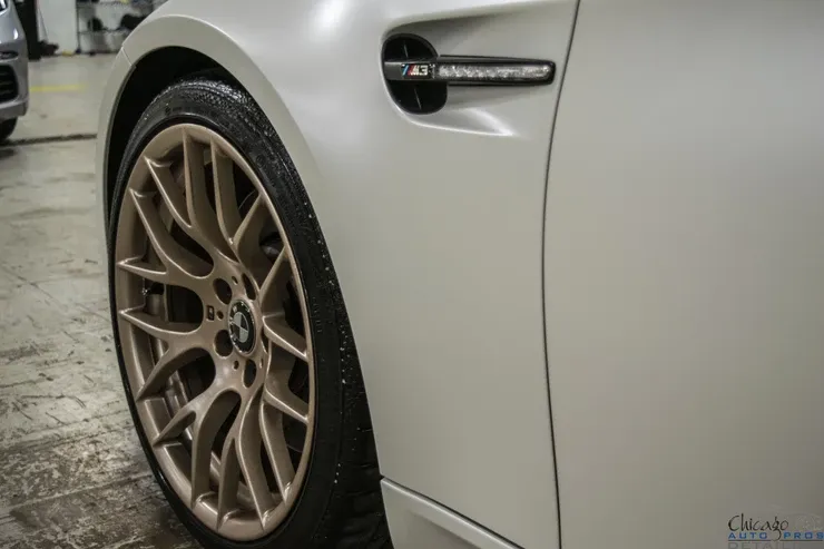 A white bmw with gold wheels is parked in a garage.