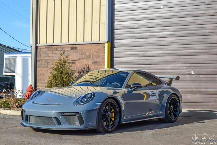 A gray porsche 911 gt3 is parked in front of a building.