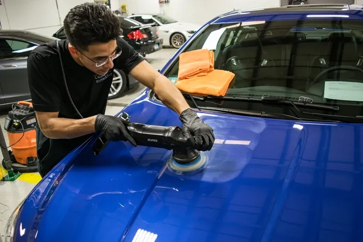 A man is polishing the hood of a blue car.