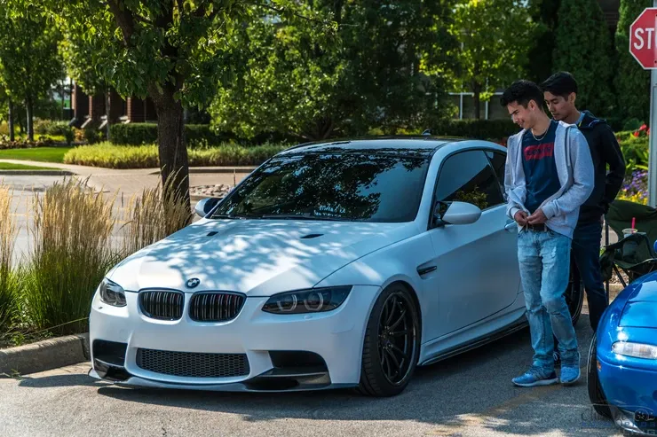 Two young men are standing next to a white bmw m3.