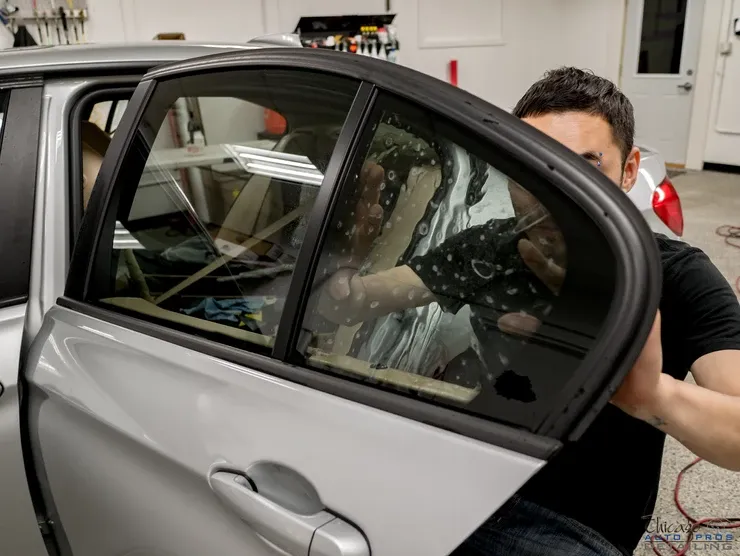 A man is applying window tinting to the back window of a car.