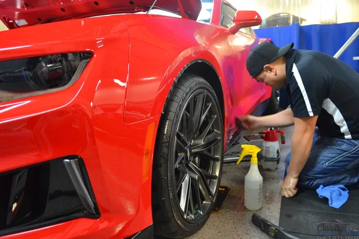 A man is kneeling in front of a red car