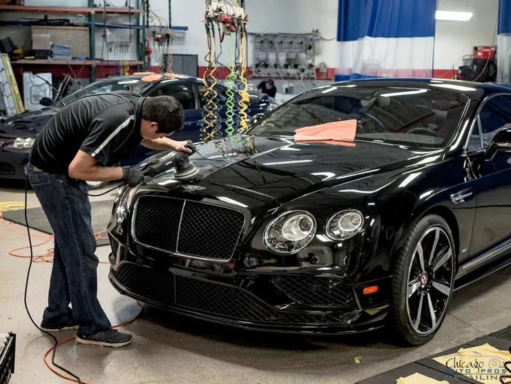 A man is polishing a black bentley in a garage.