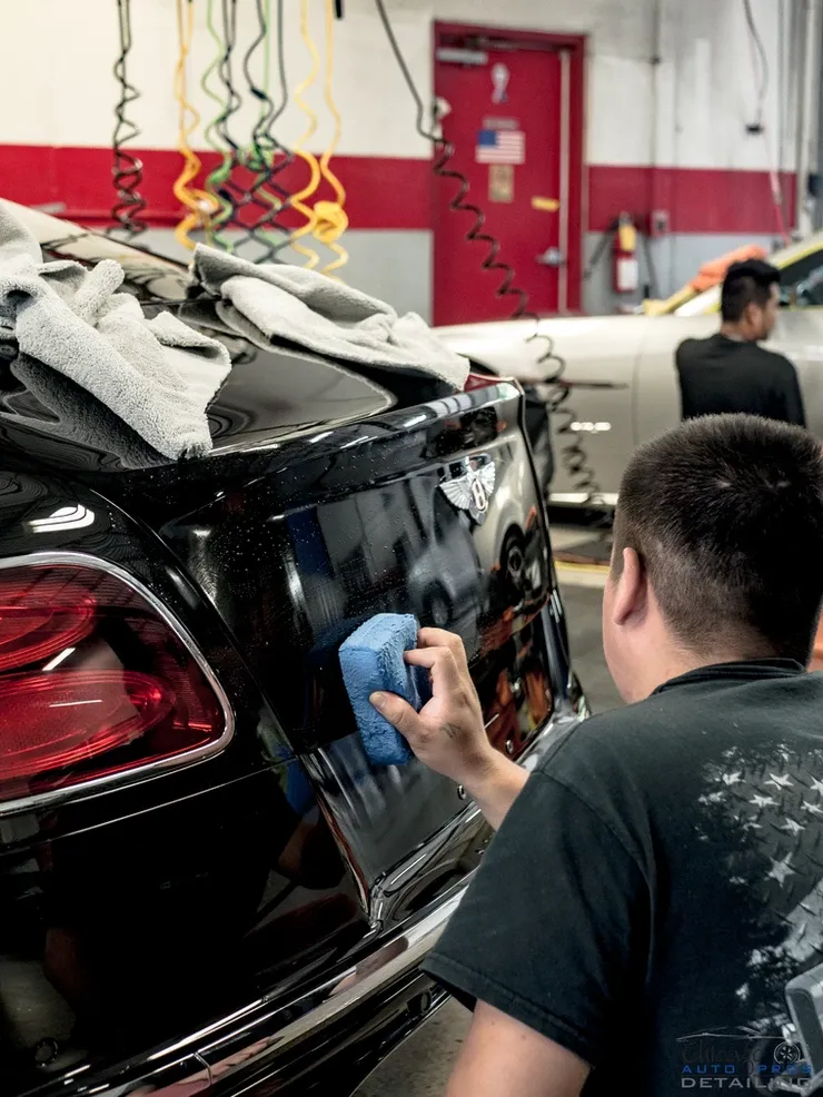 A man is polishing the back of a black car in a garage.
