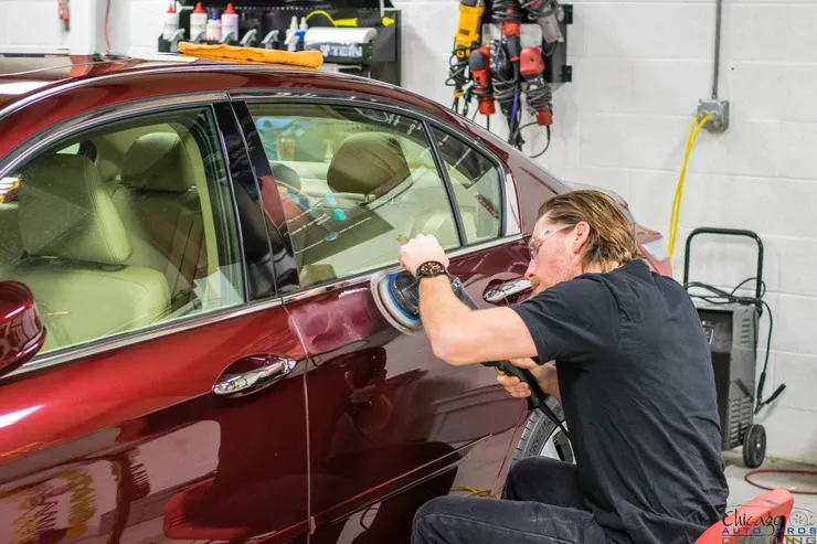 A man is polishing a red car in a garage.