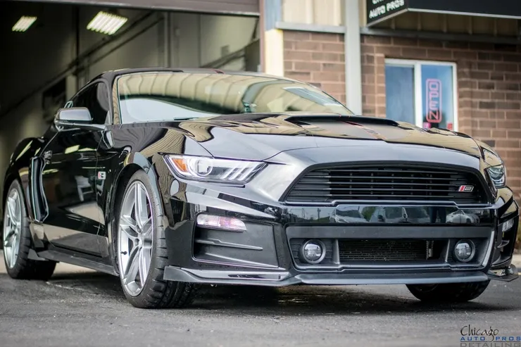 A black mustang is parked in front of a brick building.