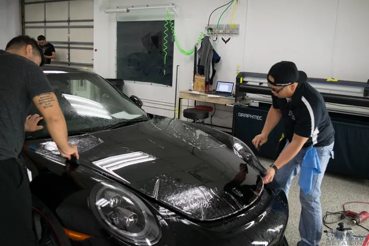 Two men are working on a black car in a garage.