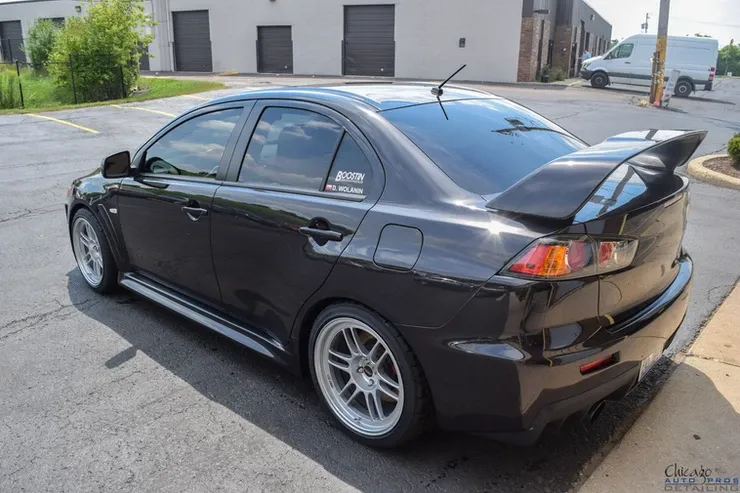 A black car is parked in a parking lot in front of a building.
