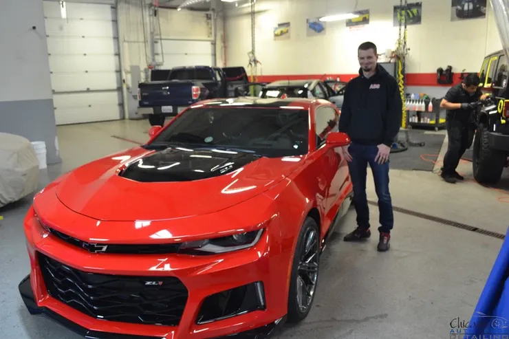 A man standing next to a red car in a garage