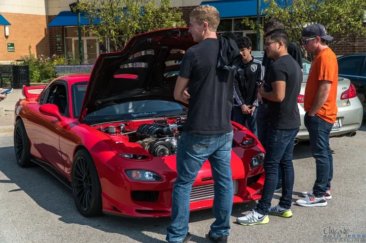 A group of men are standing around a red sports car with the hood up.