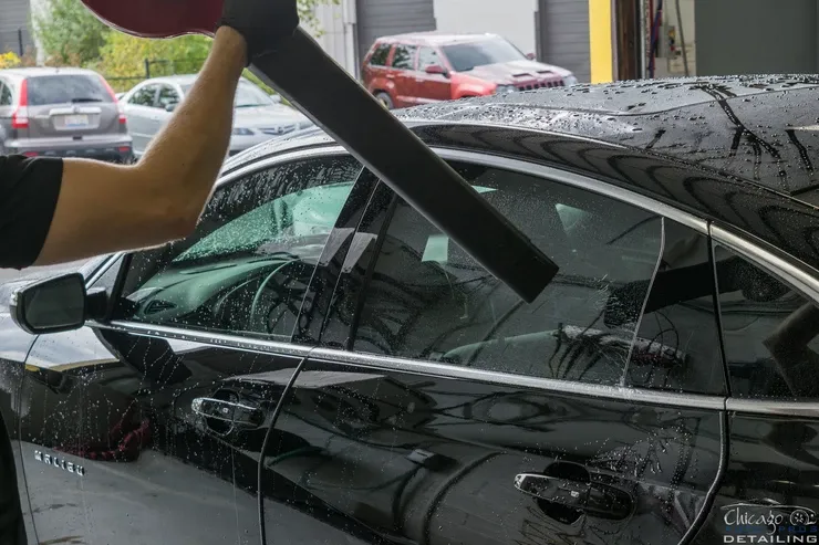 A man is cleaning the windshield of a black car.