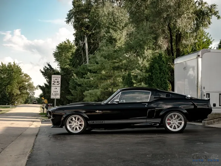 A black mustang is parked in a parking lot next to a trailer.