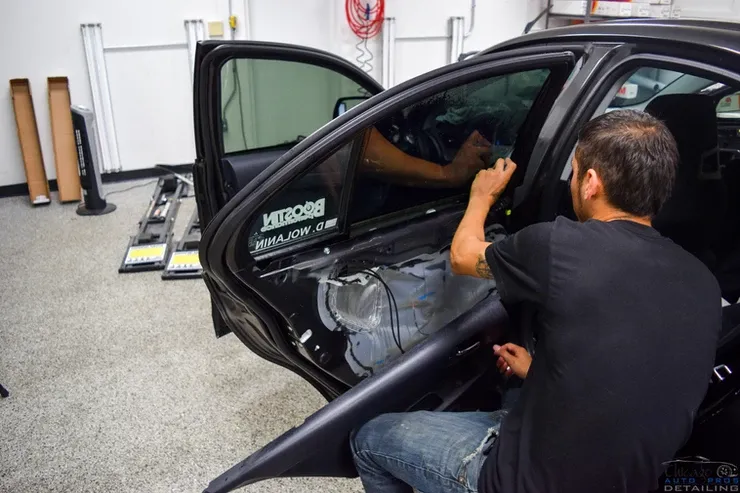 A man is installing window tinting on a car in a garage.