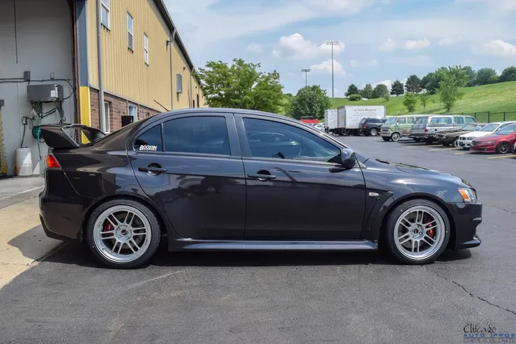 A black car is parked in a parking lot in front of a building.