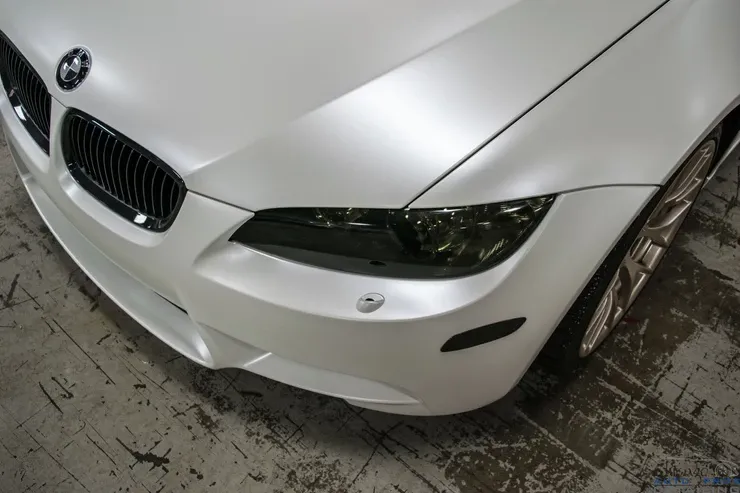 A white bmw with black headlights is parked on a concrete floor.