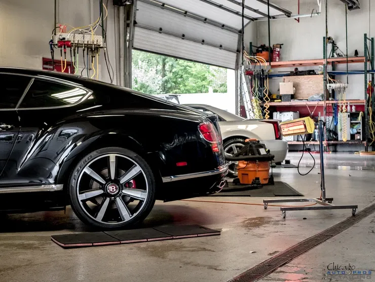 A black bentley is parked in a garage next to a white car.