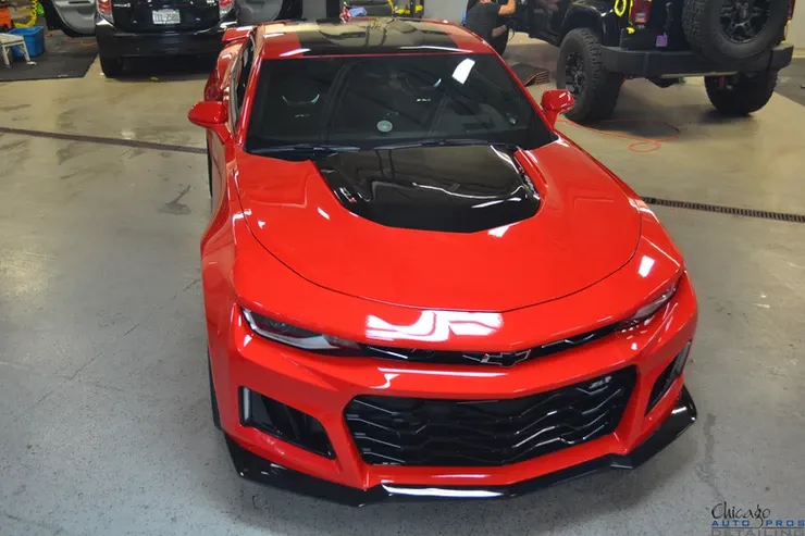 A red car with a black hood is parked in a garage