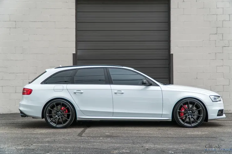 A white audi a4 is parked in front of a garage door.