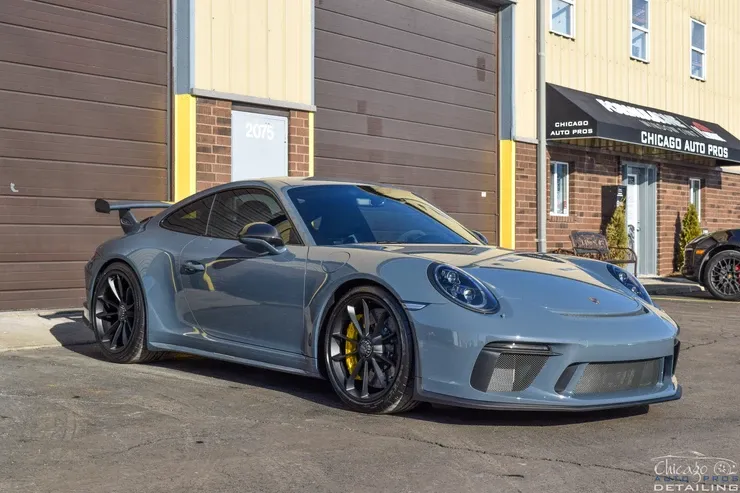 A grey porsche 911 gt3 is parked in front of a garage.