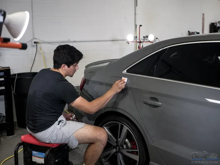 A man is sitting on a stool working on a car in a garage.
