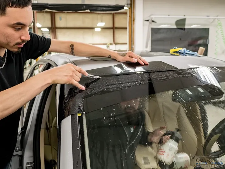A man is applying tint to the windshield of a car.