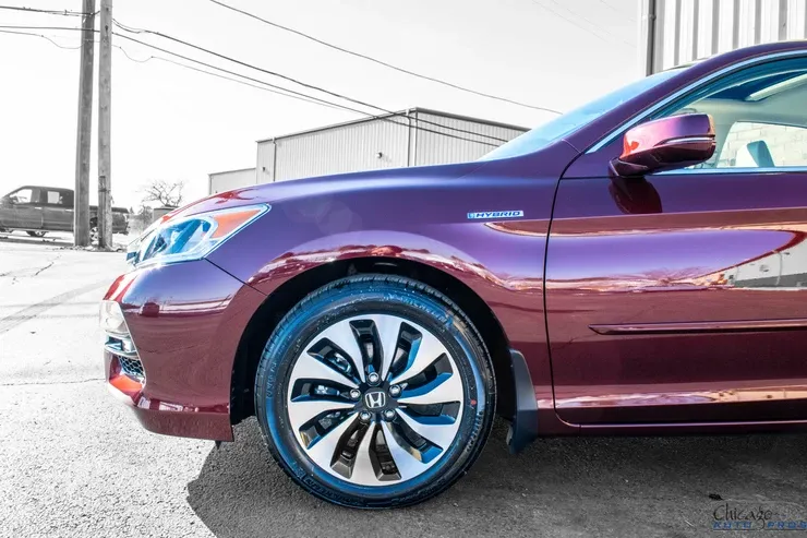 A red honda accord hybrid is parked on the side of the road.