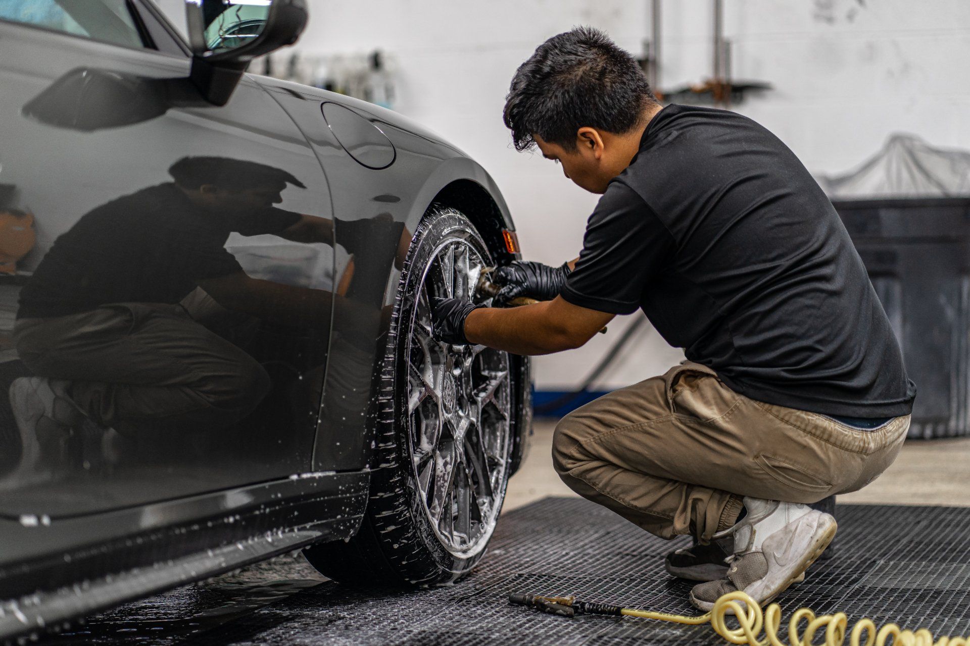 A man is kneeling down to wash the wheels of a car.