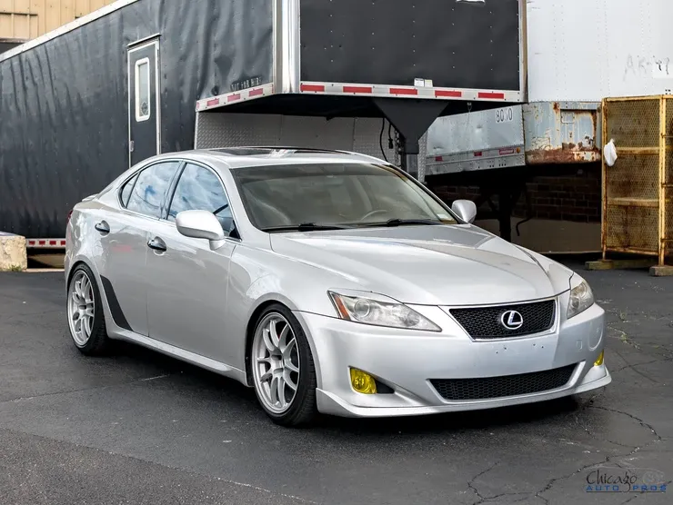 A silver lexus is parked in front of a trailer.