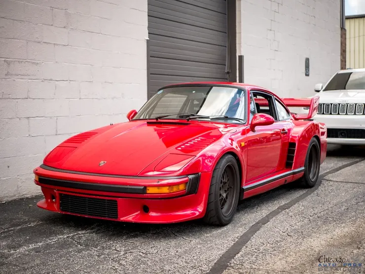 A red porsche is parked in front of a garage door.