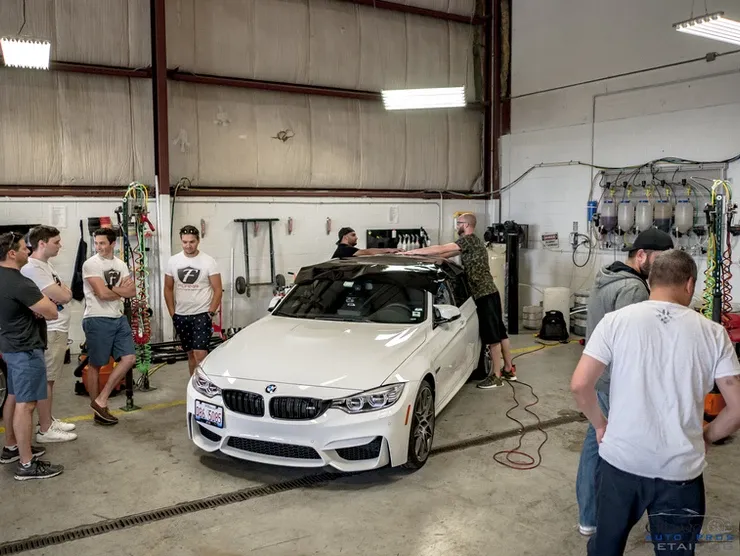 A group of men are standing around a white car in a garage.